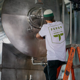 Male on a ladder wearing a white t-shirt with "Ferda American style double IPA" in green. He is also very busy at work in the brewery...
